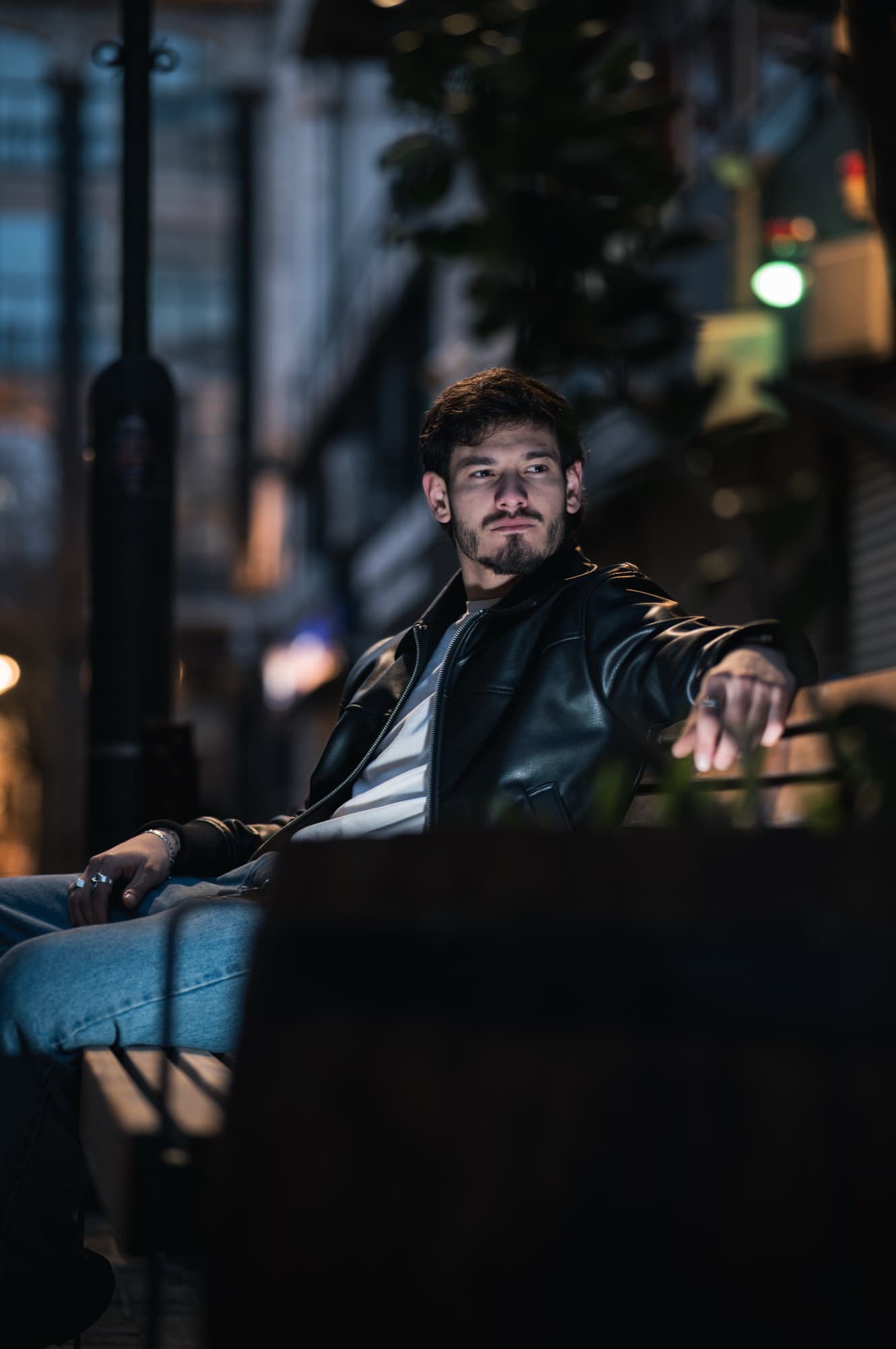 Retrato sentado en un banco con la ciudad de noche detrás