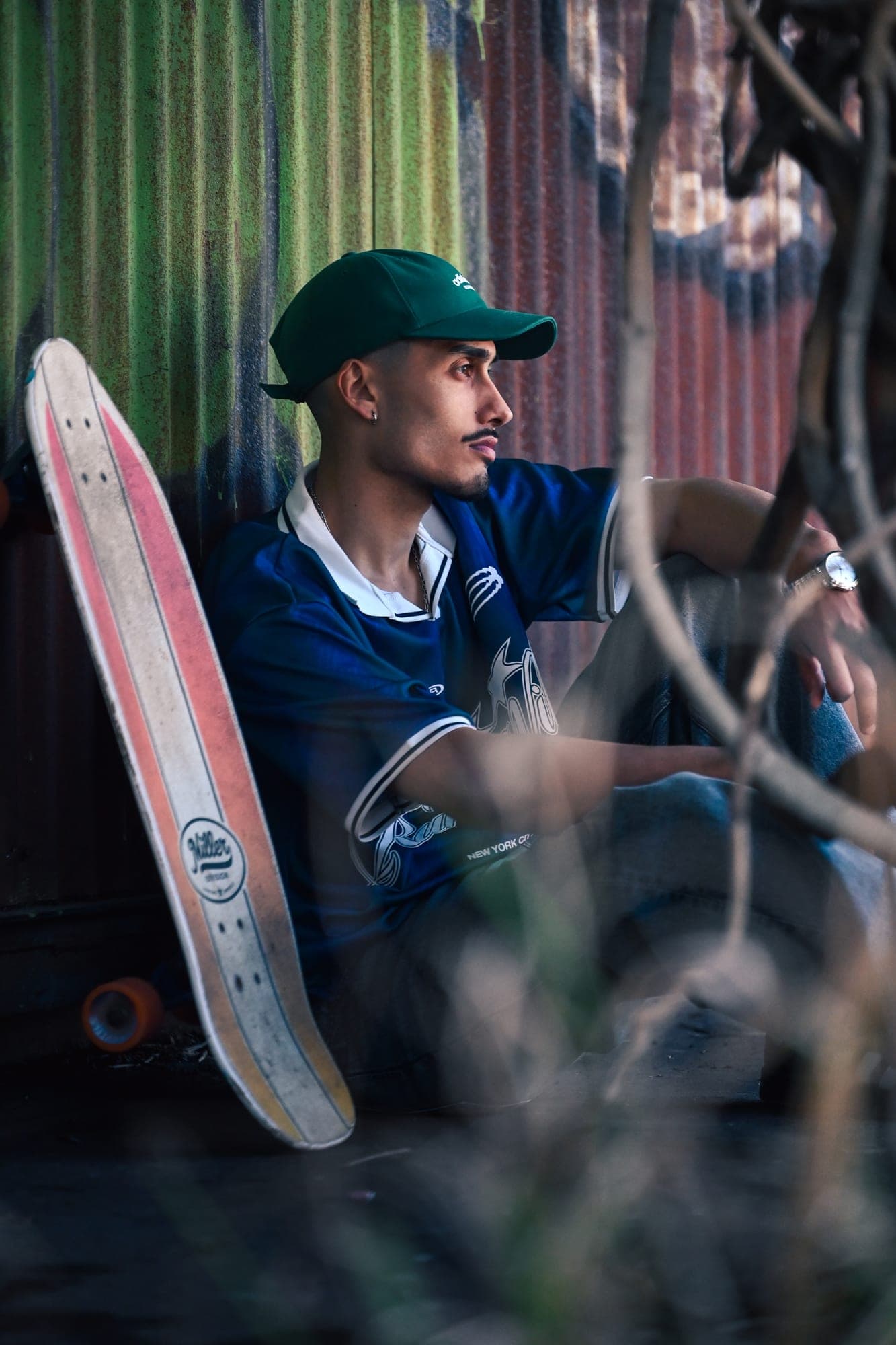 Retrato sentado junto a una tabla de skate, entre ramas y chapas pintadas